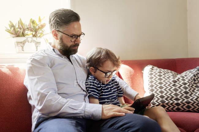 Padre y niño utilizando el dispositivo en la sala de estar - foto de stock