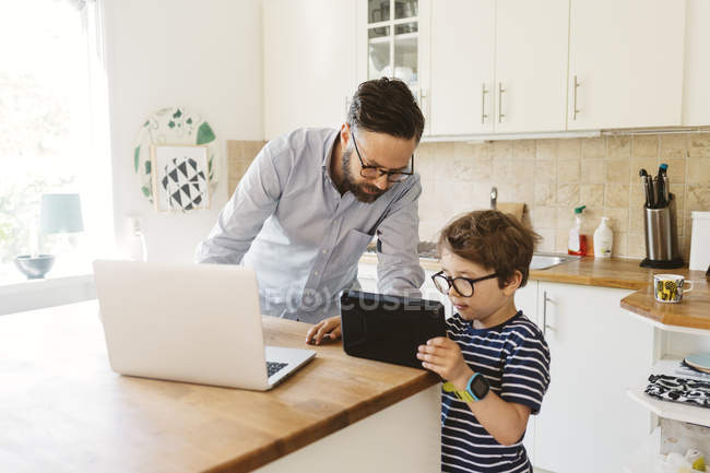 Взрослый мужчина и мальчик смотрят на планшет в домашней кухне — стоковое фото
