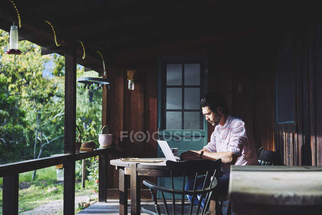 Середній дорослий чоловік використовує ноутбук на веранді, вибірковий фокус — стокове фото