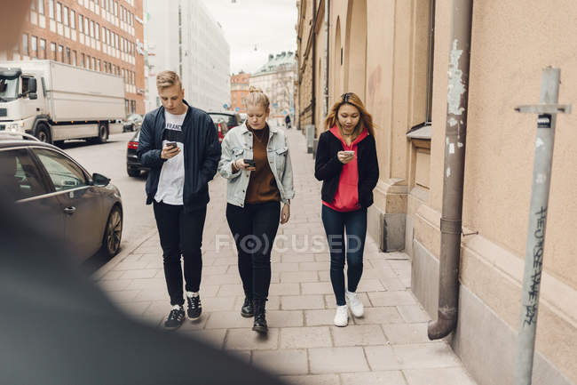 Підлітки йдуть по міській вулиці, дивлячись на телефони — стокове фото