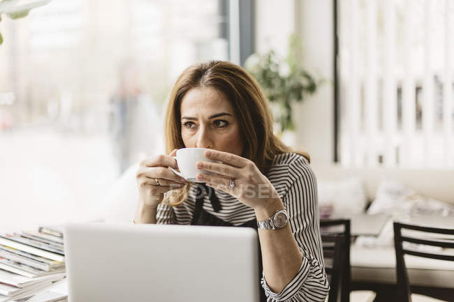 Жінка п'є каву ноутбуком в кафе, вибірковий фокус — стокове фото