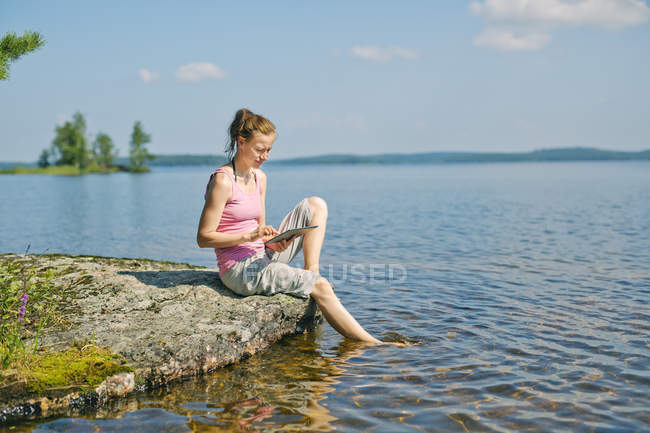 Mid adult woman using digital tablet in front of lake in Finland — Stock Photo