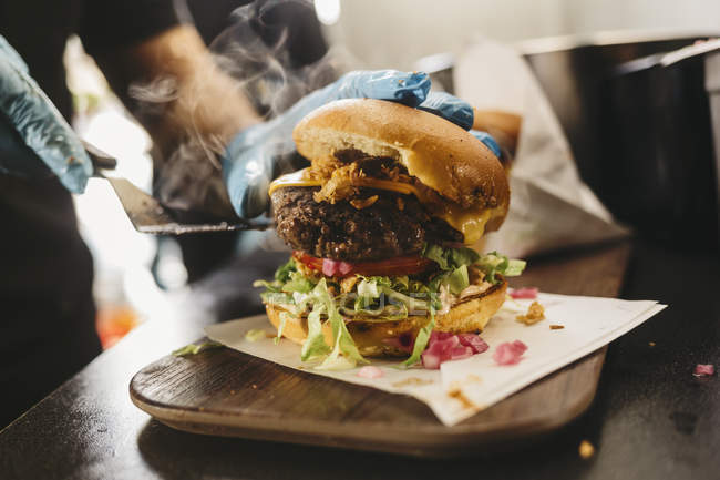 Nahaufnahme männlicher Hände in Handschuhen mit frischem Burger im Foodtruck, Fokus auf den Vordergrund — Stockfoto
