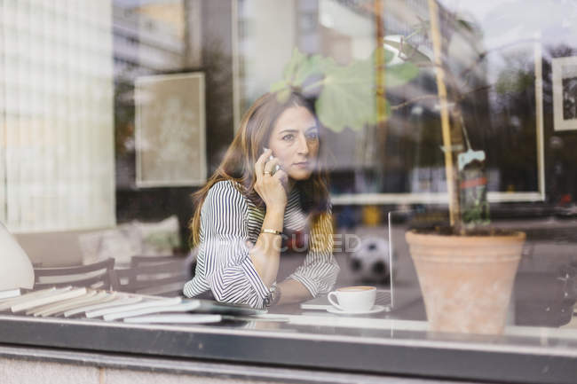 Donna che parla su smart phone dietro la finestra del caffè, messa a fuoco selettiva — Foto stock