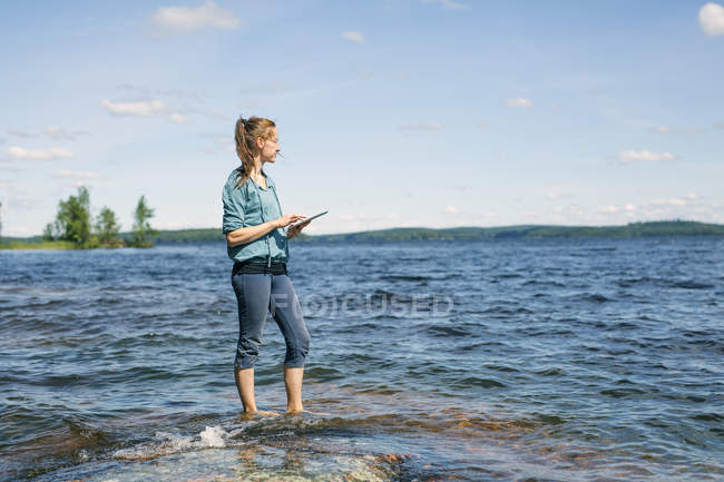 Mid adult woman using digital tablet near lake in Finland — Stock Photo