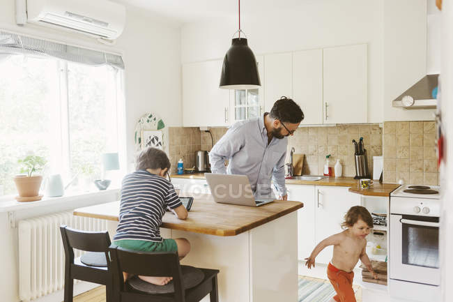 Hombre adulto medio y niños en la cocina doméstica, enfoque selectivo - foto de stock