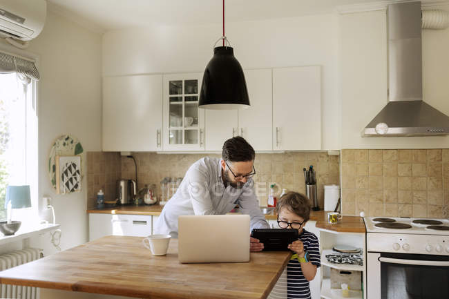 Mitte erwachsener Mann und Junge mit Blick auf Tablette in der heimischen Küche, Fokus auf den Vordergrund — Stockfoto