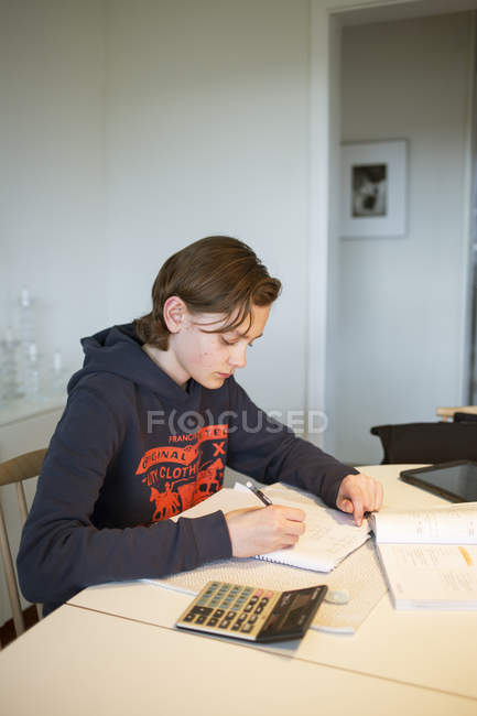 Teenage boy doing homework in house, focus on foreground — Stock Photo