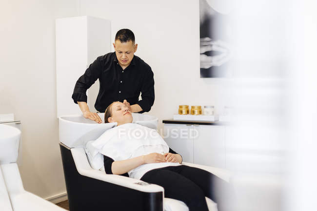 Hairdresser washing client hair, focus on foreground — Stock Photo