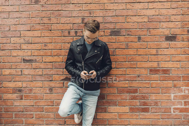 Adolescente se apoiando na parede de tijolo, usando smartphone — Fotografia de Stock
