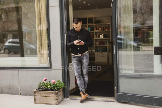 Перукар використовує смартфон біля дверей салону — стокове фото