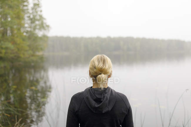 Rear view of blonde woman standing by lake, focus on foreground — Stock Photo