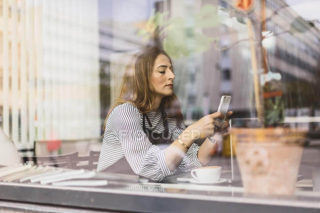 Mulher usando telefone inteligente atrás da janela do café, foco seletivo — Fotografia de Stock