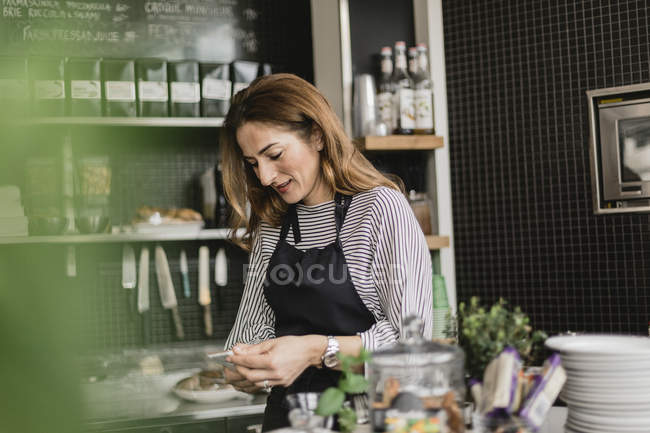 Barista utilisant un téléphone intelligent au comptoir du café, mise au point sélective — Photo de stock