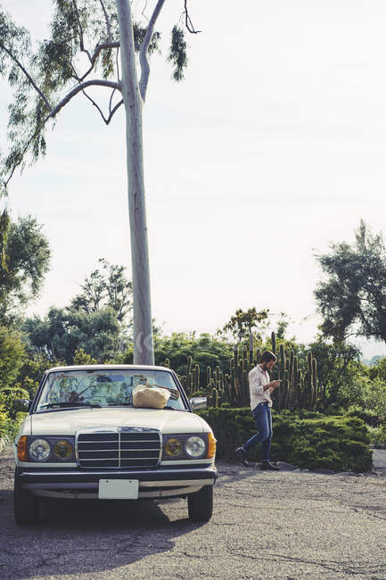 Homem adulto médio andando perto do carro e usando telefone inteligente — Fotografia de Stock