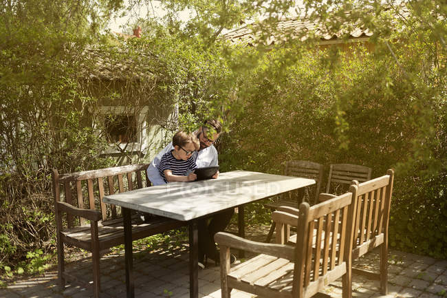 Moyen homme adulte et garçon utilisant un dispositif à la table extérieure — Photo de stock