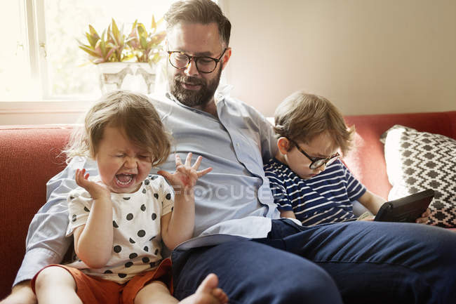 Père avec fille pleure et fils avec tablette numérique assis sur le canapé — Photo de stock