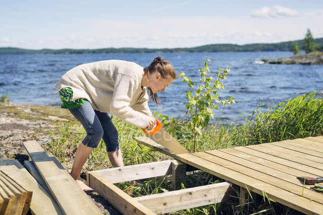 Mid adult woman building deck in front of lake in Finland — Stock Photo