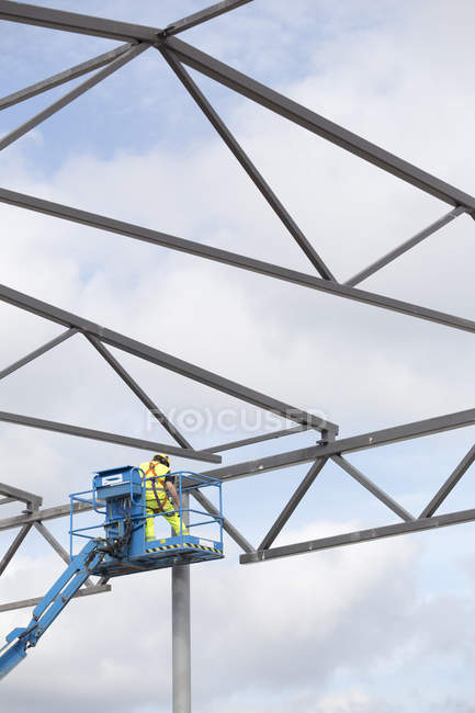 Construction worker on cherry picker by building frame — Stock Photo