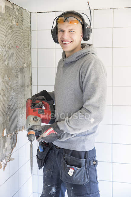Молодой человек с ушными протекторами ремонтирует дом — стоковое фото