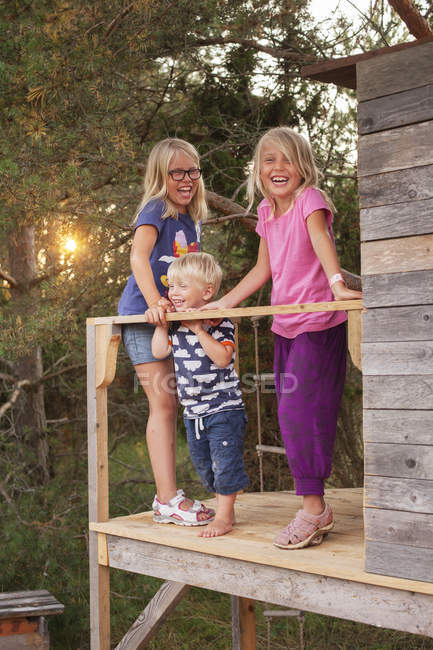 Сестри з братом на ганку дерев'яного будинку, фокус на передньому плані — стокове фото