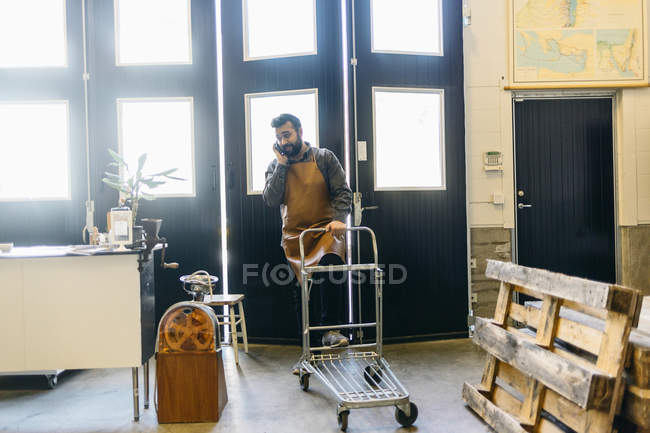 Torréfacteur de café parlant sur téléphone portable et poussant chariot — Photo de stock
