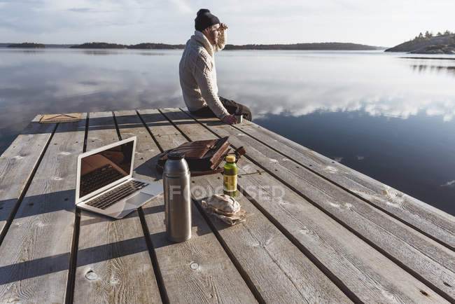 Mann auf Pier neben Laptop und Mittagessen, Fokus auf Vordergrund — Stockfoto