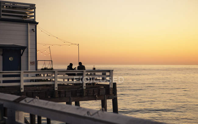 Scenic view of pier at sunset and silhouettes of people — Stock Photo