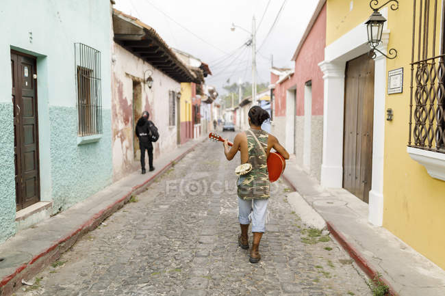Вид сзади на человека, идущего по улице с гитарой в Гуатемале — стоковое фото