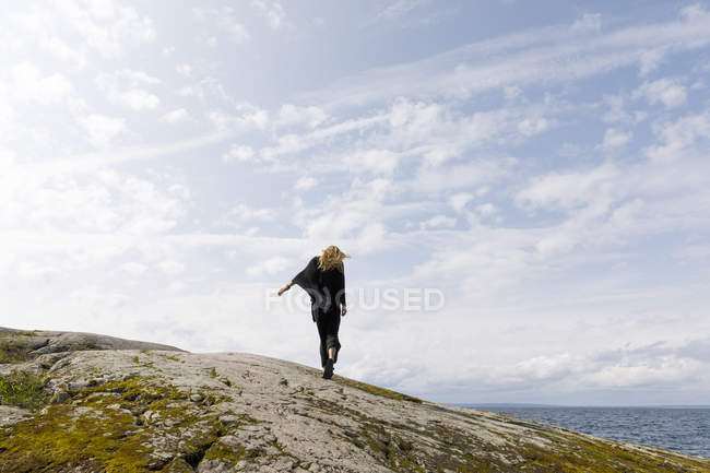 Femme balayée par le vent portant noir debout sur le rocher — Photo de stock
