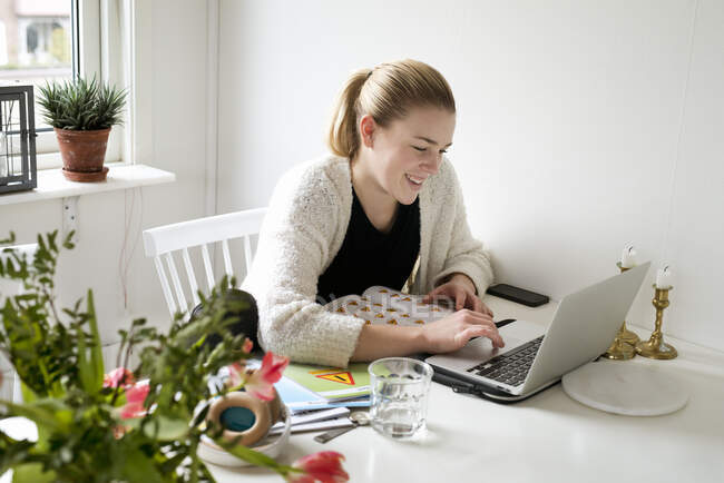 Молода жінка посміхається під час використання ноутбука — стокове фото