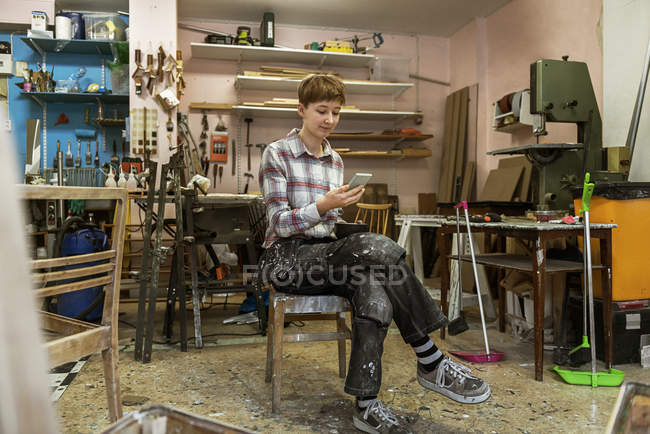 Carpinteiro usando telefone inteligente na oficina — Fotografia de Stock