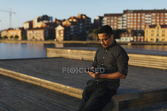 Mann sitzt auf Promenade und benutzt Smartphone — Stockfoto