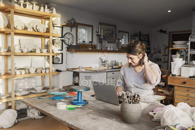 Woman using laptop in pottery workshop — Stock Photo