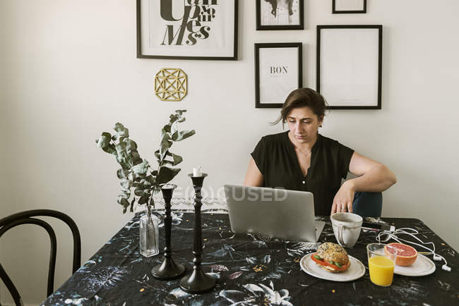 Jovem mulher usando laptop durante o café da manhã — Fotografia de Stock