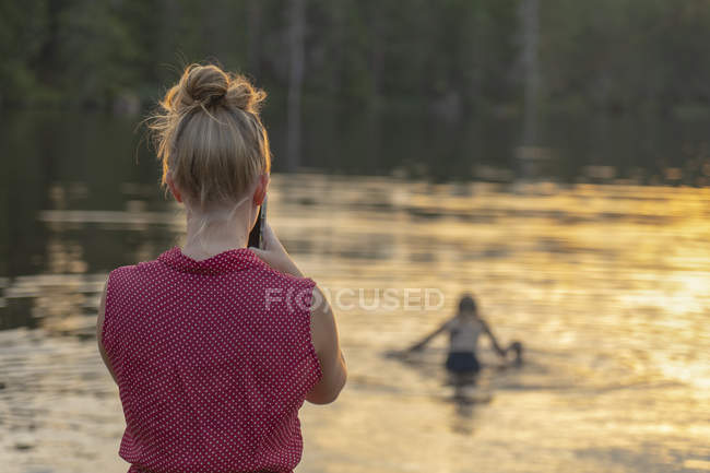 Жінка фотографує дівчину в озері на заході сонця, вибірковий фокус — стокове фото