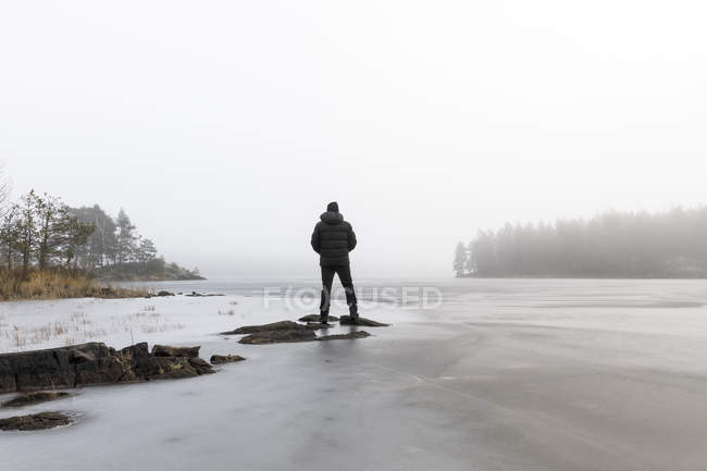 Hombre sobre rocas en lago congelado en Lotorp, Suecia - foto de stock
