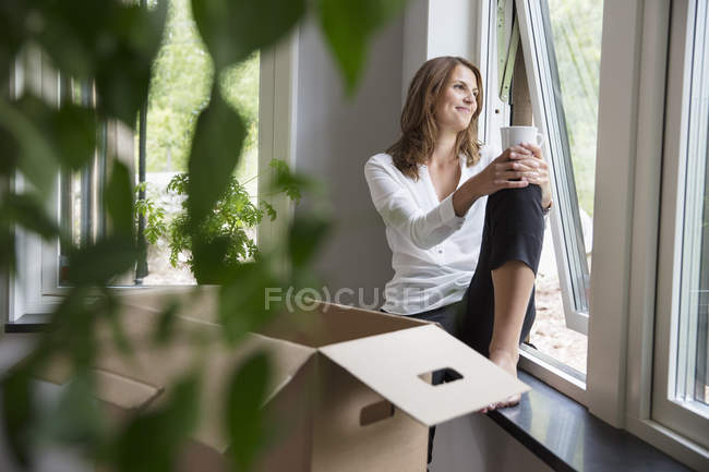 Mujer sentada en el alféizar de la ventana con taza de café - foto de stock