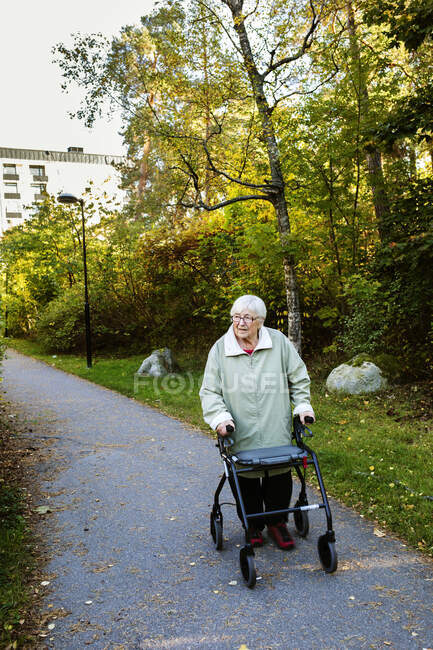 Femme âgée utilisant un cadre de marche et marchant dans le parc — Photo de stock