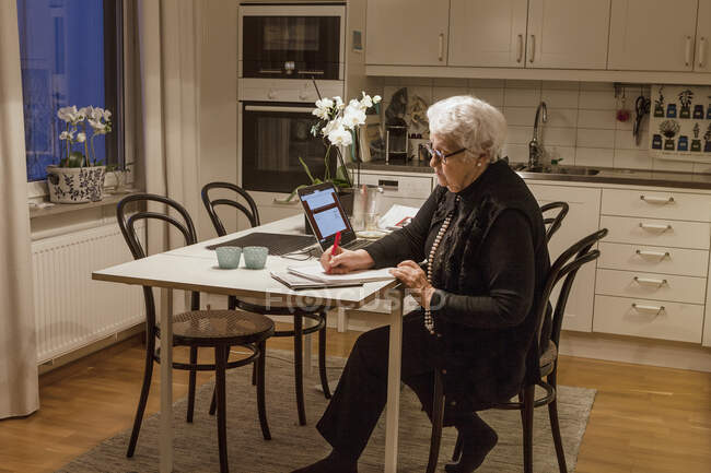 Femme âgée utilisant un ordinateur portable dans la cuisine — Photo de stock