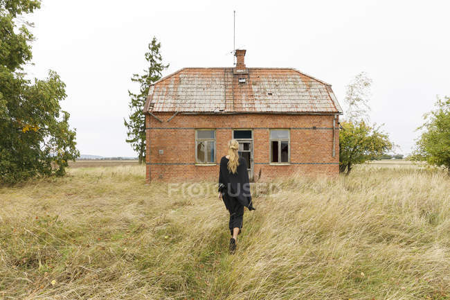 Frau läuft zu verlassenem Haus — Stockfoto
