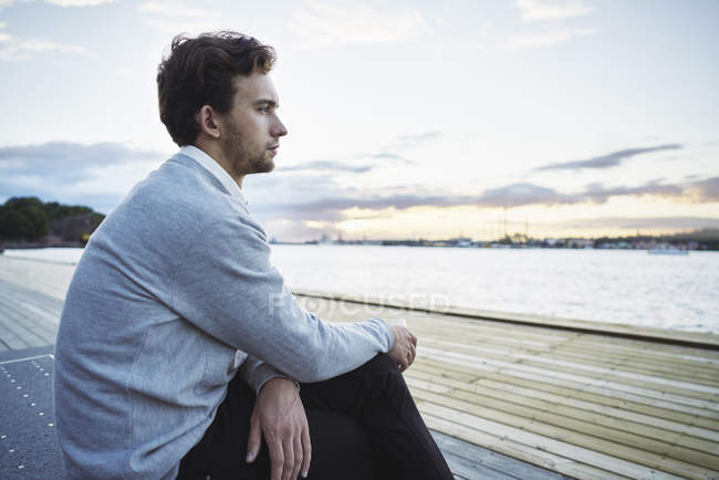Молодий чоловік, що сидить біля моря, зосереджений на розбірливості. — стокове фото