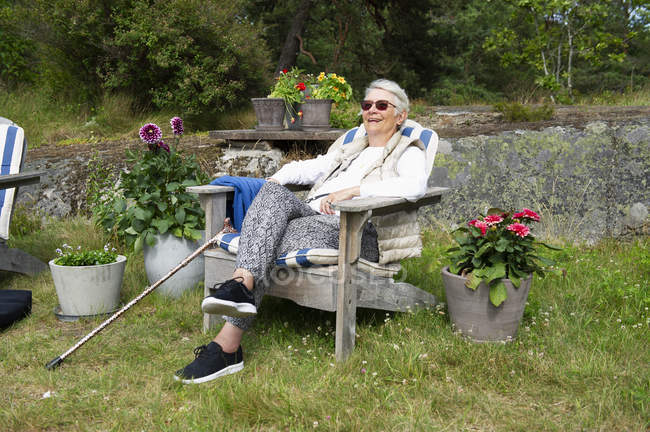Mulher sênior sentada na cadeira do convés no jardim — Fotografia de Stock
