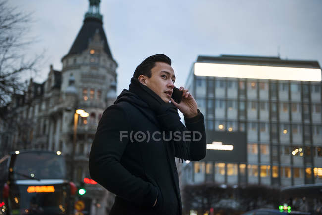 Young man talking on cell phone while walking down city street — Stock Photo