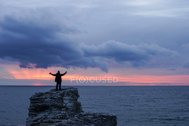 Silueta del hombre en la roca por el mar al atardecer - foto de stock