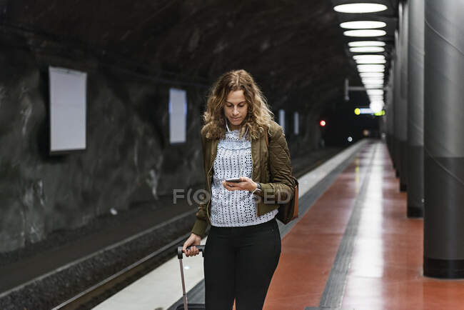 Mulher nova com mala usando smartphone na estação de metrô — Fotografia de Stock