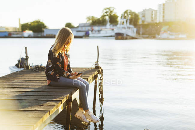 Woman sitting on jetty and using smart phone — Stock Photo