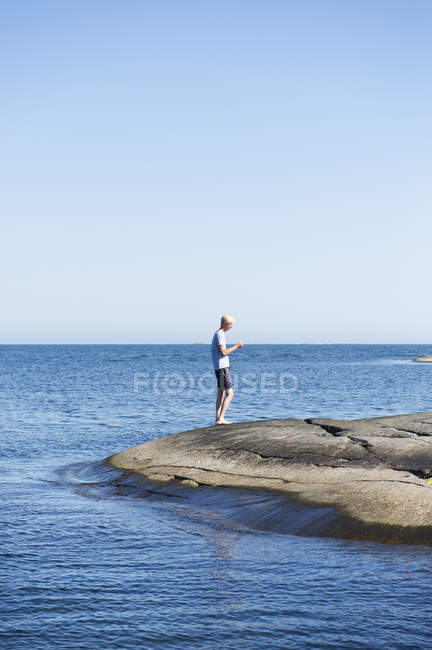 Young man standing on rocks by sea — Stock Photo