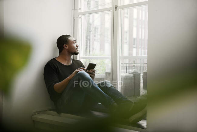 Чоловік середнього віку використовує смартфон на підвіконні — стокове фото