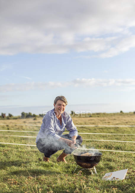 Woman crouching by brazier in field — Stock Photo